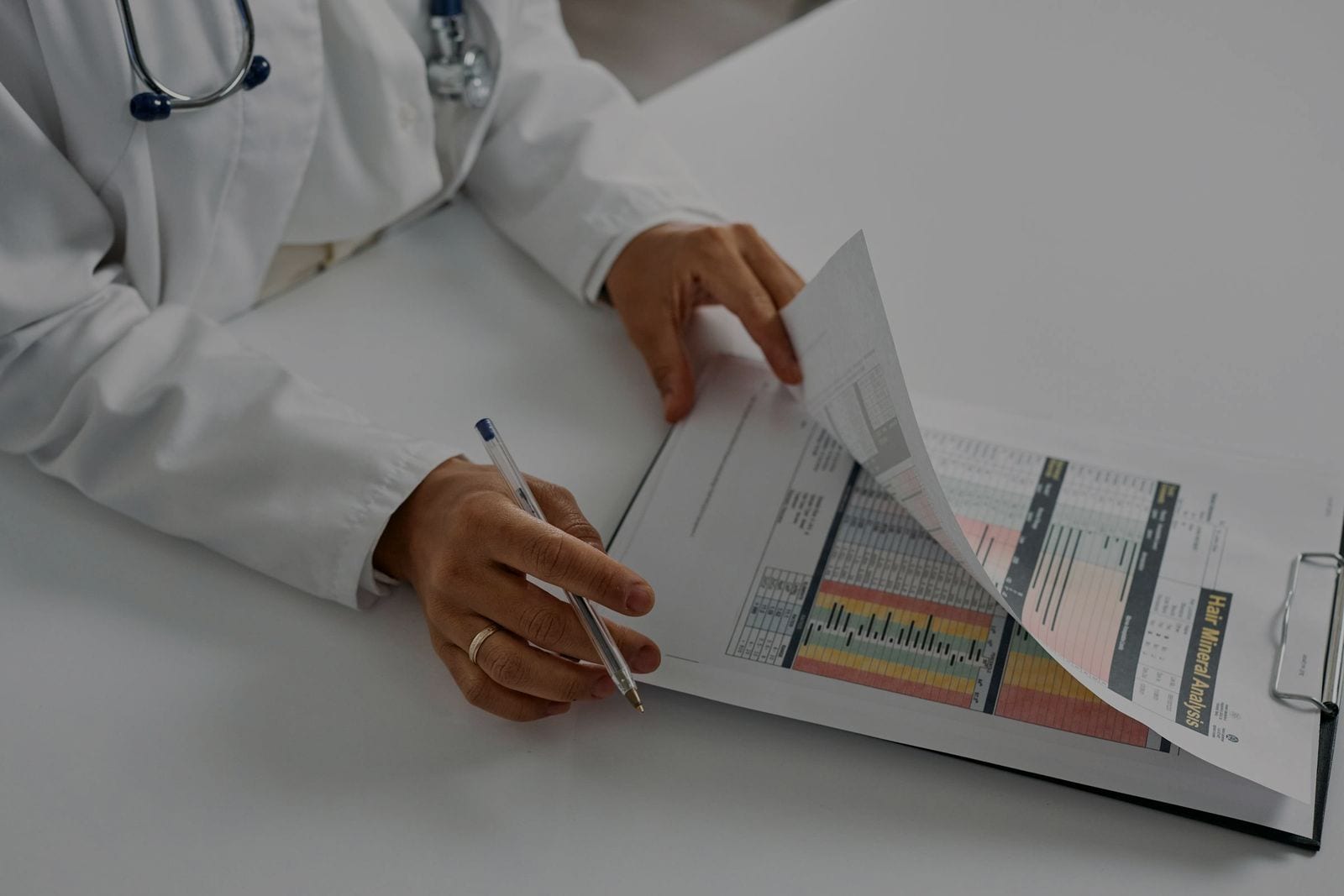 A doctor's hands holding a notepad and pen — taking notes from a printed report.